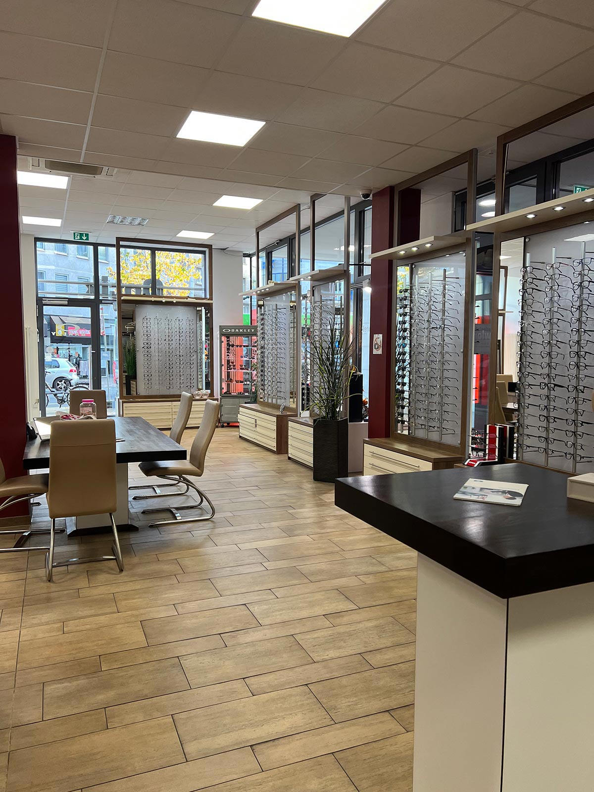 Ein moderner Optikerladen mit beigen Stühlen, Holzfußboden und großen Fenstern