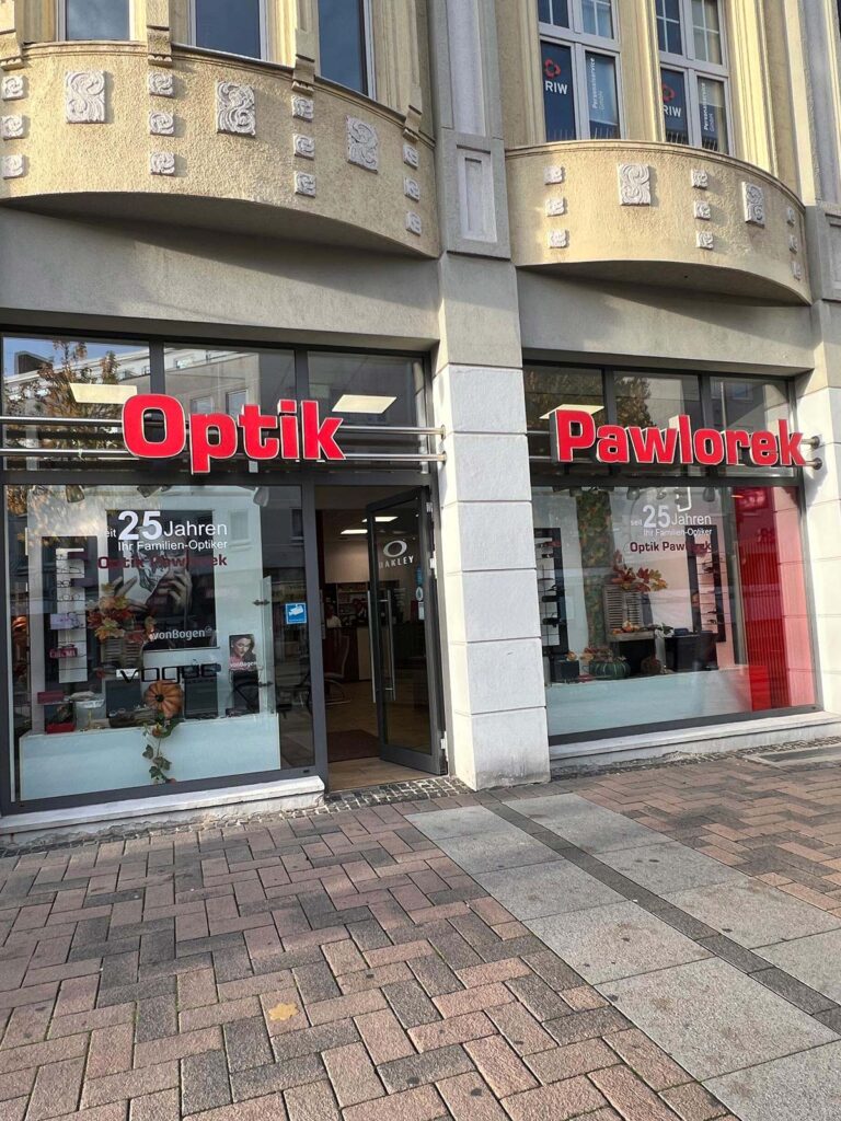 Große Glasfassade eines Optikergeschäfts mit roter Schrift und heller Fassade