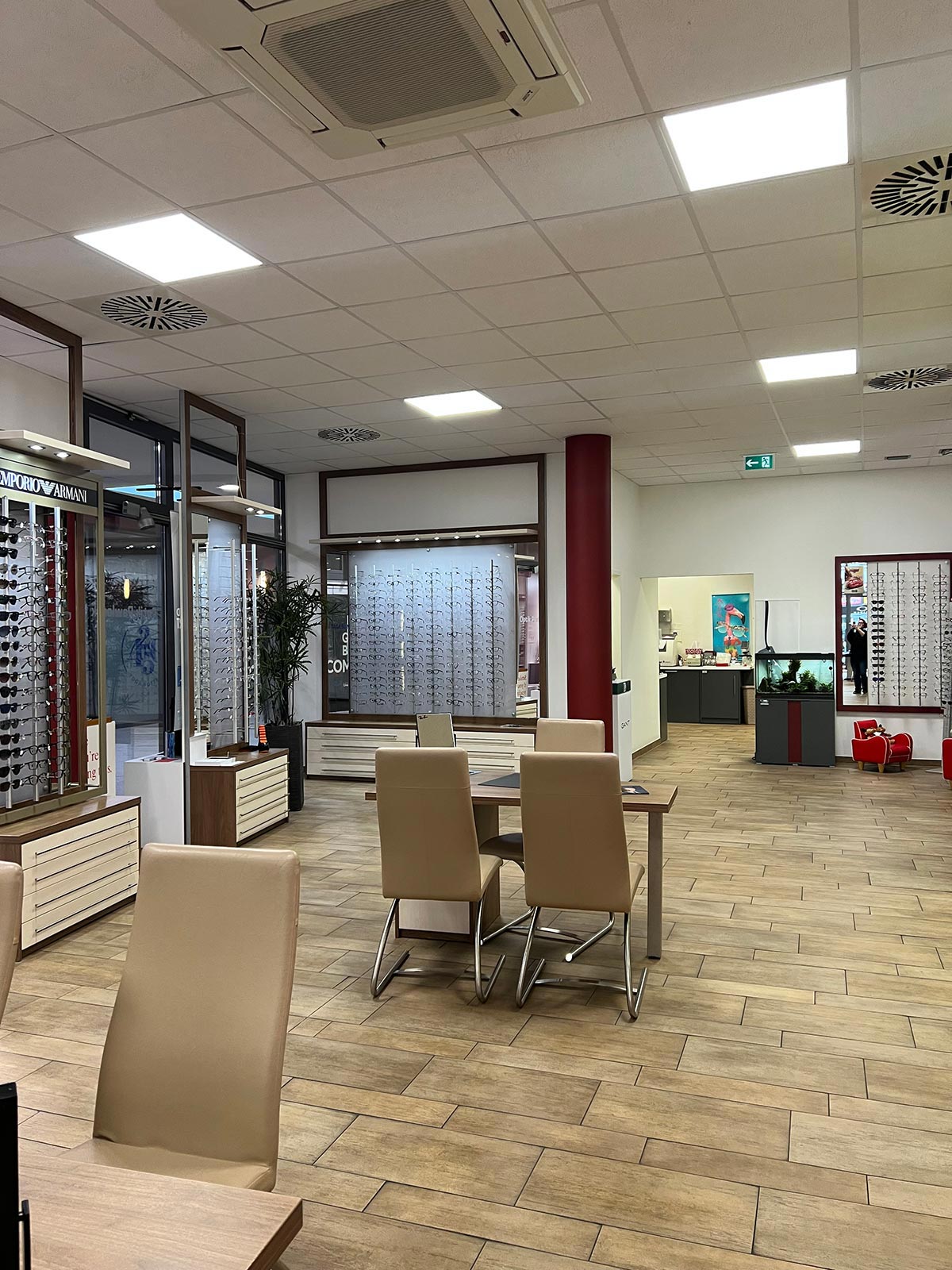 Modern Optikergeschaeft mit beigen Stuehlen, Holzmoebel, Brillendisplays und Pflanzen